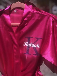 a pink robe with the word kaleaah on it is hanging from a hanger