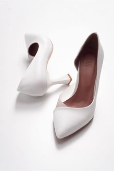 a pair of white high heel shoes on top of a white surface with one shoe in the middle