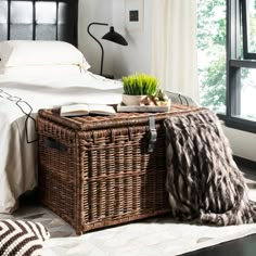 a wicker basket on top of a bed next to a lamp and window sill