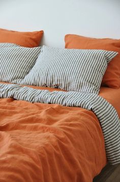 an orange and white bed with two pillows on top of it, next to a wall