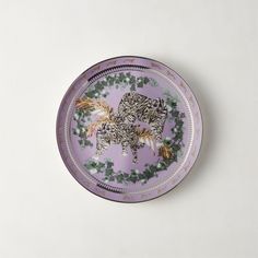 a purple plate with two cats on it and green leaves around the edge, sitting on a white surface