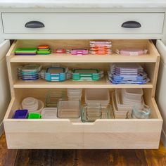 an open drawer in a kitchen filled with plastic containers and dishes on the bottom shelf