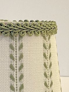 a close up of a lamp shade on a white surface with green trimmings