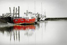 two boats are docked in the water near each other and one boat is red with white writing on it