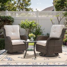 two wicker chairs sitting on top of a rug in front of a white fence