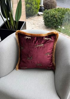 a red pillow sitting on top of a chair next to a potted green plant