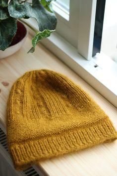 a yellow knitted hat sitting on top of a window sill next to a potted plant