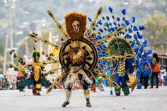 some people in costume are walking down the street with feathers on their head and one is wearing a lion mask