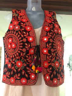 This is a beautiful Indian colorful vest. It is primarily full of red and gold embroidery throughout the piece. It has lovely embroidered designs throughout the piece in both red and gold adorned with small foil mirrors.  There is a tie up in the front as shown with beads and pom poms on the end, the pom poms each have a single bead in them as well.. The back of the vest is plain black except about 7.5 cm (2.95 in) of embroidery at the base.  This is a lovely piece to wear on top of traditional Festive Bohemian Vest With Floral Embroidery, Traditional Vest With Floral Embroidery For Festival, Traditional Floral Embroidered Vest For Festival, Bohemian Black Embroidered Vest, Traditional Embroidered Festive Vest, Folk Style Embroidered Choli For Festive Occasions, Folk Style Festive Vest With Floral Embroidery, Festive Embroidered Vest With Multicolor Embroidery, Bohemian Embroidered Festival Vest