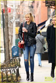 the blonde woman is walking down the street with her hand in her pocket and holding a red purse