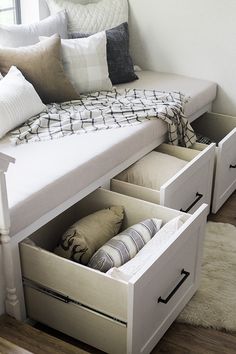 a white bed with drawers underneath it in a room next to a couch and window