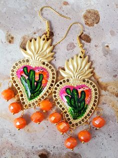 Detailed and beautiful artistically painted earrings, they are painted in detail taking a miniature painting of a cactus in green tones, with a sky in pink, yellow and orange colors, adorned with glass beads, the hooks are hypoallergenic, the earrings are protected with Several layers of high-quality jewelry varnish, improving the quality and durability of the earrings' paint. These earrings are inspired by our Mexican culture and hand painted; They are the ideal gift because they combine with any outfit both day and night, enhancing the beauty of whoever gets them and attracting attention for being unique hand-painted pieces, the Ideal gift for Mother's Day and holidays. Features/ Product info Note: Each earring is hand painted, there are small differences between each pair, so each pair Multicolor Hand Painted Jewelry For Festivals, Artsy Dangle Jewelry For Festivals, Artistic Dangle Jewelry For Festivals, Artisan Hand Painted Jewelry For Festivals, Artistic Earrings For Festivals, Hand Painted Gold Jewelry For Festival, Hand Painted Artsy Jewelry For Festivals, Handmade Artistic Beaded Earrings, Handmade Adjustable Drop Heart Earrings