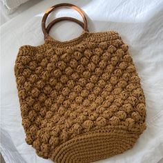 a brown crocheted purse sitting on top of a white bed next to a wooden handle