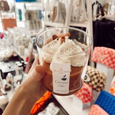 a person holding up a cupcake with whipped cream and cinnamon on top in a store