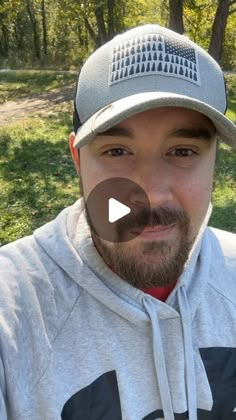 a man with a beard wearing a grey hoodie and a baseball cap in the park