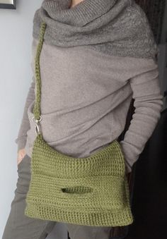 a woman is holding a green purse with holes in the front and bottom, while standing next to a wall