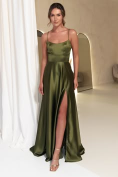 a woman standing in front of a white backdrop wearing a green dress and high heels