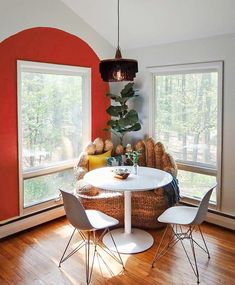 a dining room with red walls and white chairs around a round table in front of two large windows