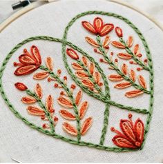 an embroidered heart with red flowers on green thread in front of a white wall hanging