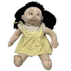 a stuffed doll with black hair wearing a yellow dress