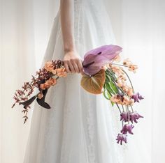 a woman in a white dress holding a bouquet of purple and orange flowers on her wedding day