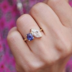 a woman's hand holding a ring with two pear shaped blue and white stones