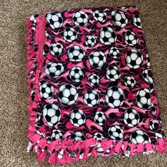 a pink and black blanket with soccer balls on it sitting on the floor next to a carpet