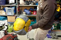 a man holding a yellow and gray bag in his hand while standing next to a shelf full of backpacks