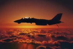 a fighter jet flying over the clouds at sunset