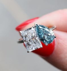 a woman's hand is holding an engagement ring with two blue and white diamonds