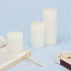 three white candles sitting next to an open book and matchsticks on a blue background