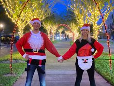 two people dressed as santa and mrs claus holding hands in front of christmas lights on trees