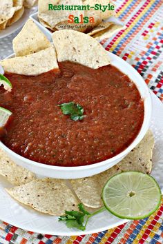 a white bowl filled with salsa surrounded by tortilla chips and lime wedges