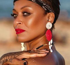 a woman with tattoos on her chest wearing red and white earrings, looking off to the side