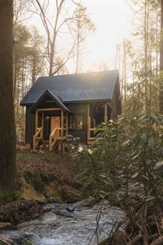 a small cabin in the woods with a stream running through it's foreground