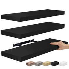 a hand is holding the edge of a black shelf with four different colors and sizes