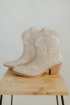 a pair of white cowboy boots sitting on top of a wooden table