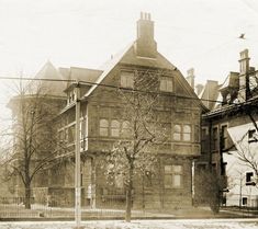 an old photo of a large building on the corner of a street with trees in front of it