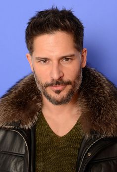 a man with a goatee and leather jacket looking at the camera while standing in front of a blue background