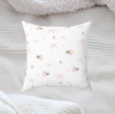 a white pillow with pink bows on it sitting on a bed next to a teddy bear