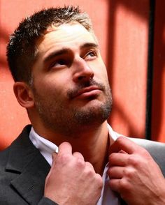 a man is adjusting his tie in front of a red wall with sunlight coming through the window