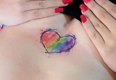 a woman's stomach with a rainbow heart tattoo on her chest and two hands