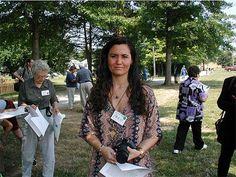 a woman holding papers in her hands while standing next to other people on the grass