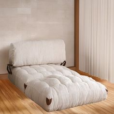 a white futon bed sitting on top of a wooden floor next to a window