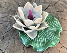 a small ceramic flower sitting on top of a leafy green plate in the shape of a lotus