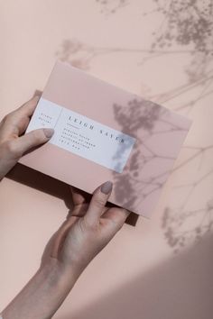 a person holding up a business card in front of a pink wall with shadows on it