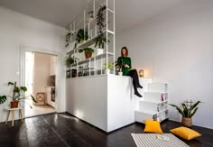 a woman sitting on top of a white shelf next to a living room filled with plants