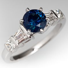 This beautiful ring is centered with one (1) round brilliant cut natural sapphire weighing 1.30 carats that is set into a six-prong head. The shoulders of the ring are each accented with two (2), channel set, tapered baguette cut diamonds and one (1), channel set, princess cut diamond. The ring measures 7.9mm at the top, rises 8.5mm above the finger, tapering to 1.8mm wide and 1.2mm thick at the base of the shank. This ring is currently a size 6.75. Classic Gia Certified Sapphire Ring, Luxury Diamond Ring With Brilliant Cut Lab-created Sapphire, Elegant Sapphire Ring With Prong Setting For Proposal, Luxury Lab-created Sapphire Ring With Prong Setting, Elegant Round Cut Sapphire Ring For Proposal, Classic Sapphire Ring With Moissanite Accent Stones, Dazzling Brilliant Cut Sapphire Ring In Platinum, Sapphire Ring With Brilliant Cut For Proposal, Luxury Round Cut Sapphire Proposal Ring