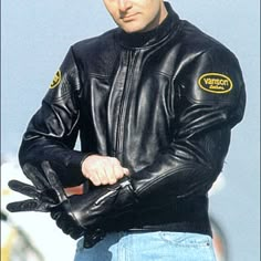 a man wearing a black leather jacket and blue jeans is holding his hands in his pockets