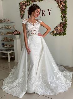 a woman in a white wedding dress standing next to a floral wall with flowers on it